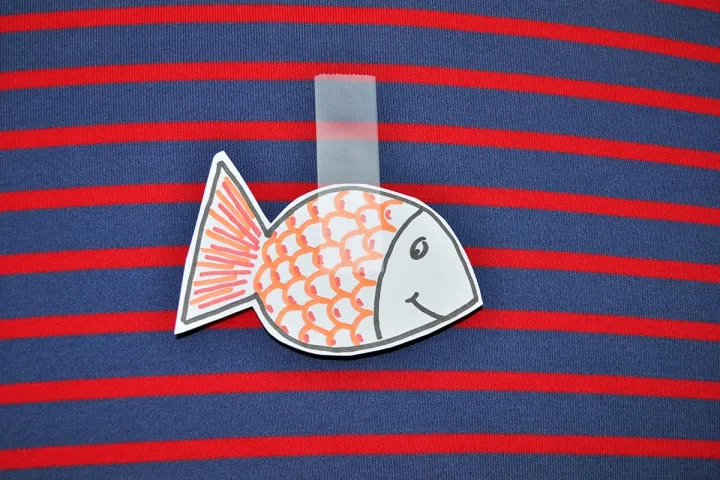A paper fish cutout taped to a striped blue and red fabric, referencing the French April Fools' tradition.