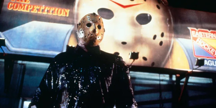 Jason Voorhees in hockey mask and black wet clothing stands before a large hockey mask backdrop.