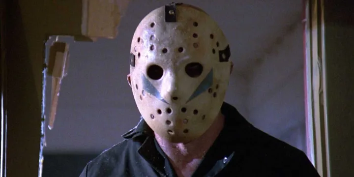 Close-up of Jason Voorhees wearing his iconic weathered hockey mask, framed in a doorway.