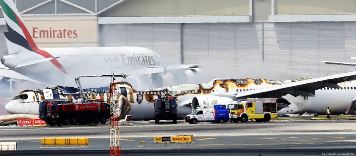 Emirates airplane engulfed in flames on airport runway with emergency vehicles responding.