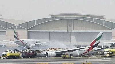 Emirates aircraft on fire at airport with firefighting vehicles spraying water, hazy conditions.