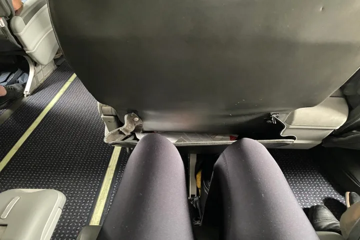 Close-up view of cramped economy airplane seat legroom from a passenger's perspective.