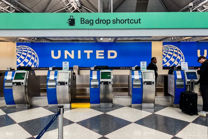 United Airlines bag drop shortcut check-in kiosks at an airport terminal with travelers.