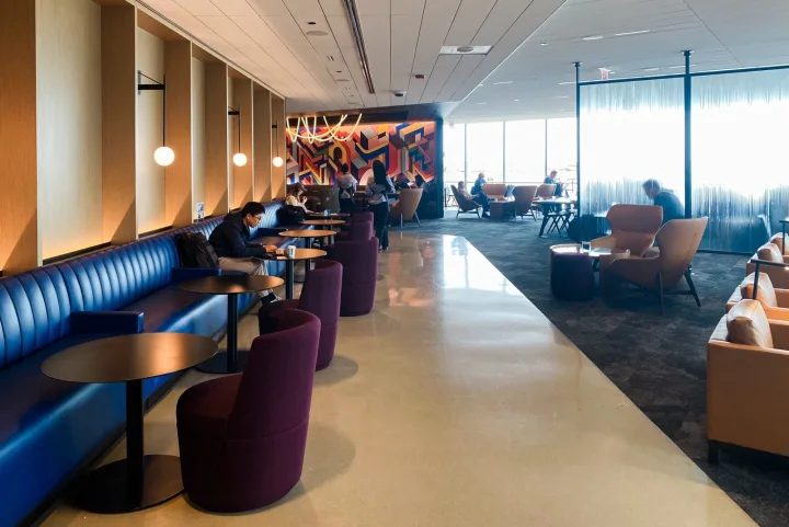 Spacious upscale airline lounge interior with blue leather seating and colorful wall art.