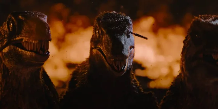 Three dark raptors with open jaws face the camera against a fiery orange explosion backdrop.