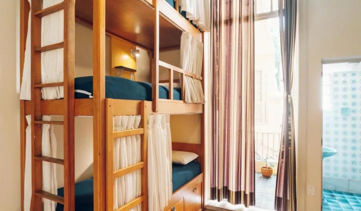 Neat wooden bunk beds with privacy curtains in a hostel dormitory room.