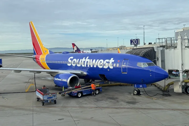 A Southwest Airlines Boeing 737 in blue livery parked at a gate on a sunny airport tarmac.