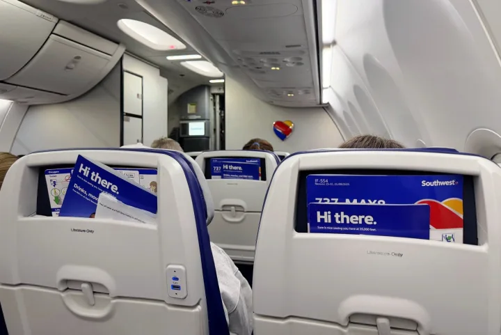Interior of a Southwest Airlines 737 MAX cabin showing blue seats with seatback screens displaying 'Hi there.'