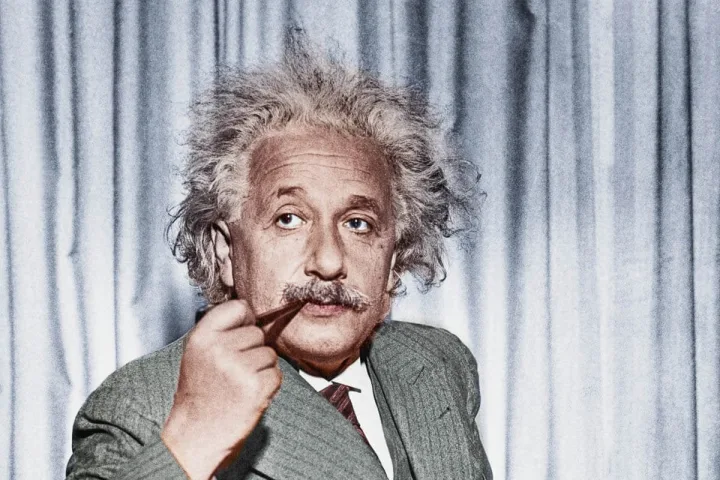 Colorized portrait of Albert Einstein holding a pipe, looking directly at camera.