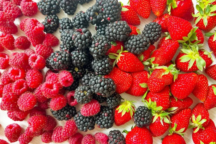 Colorful assortment of fresh raspberries, blackberries, and strawberries displayed on a flat surface.