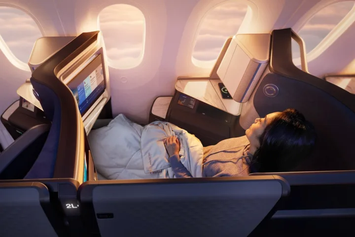 Woman reclined in a lie-flat business class seat with duvet inside a premium aircraft cabin.
