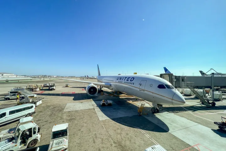 United Airlines Boeing 787 Dreamliner parked at an airport gate under clear blue sky.