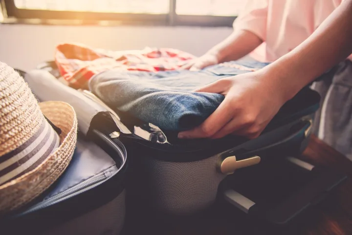 Person packing clothes and accessories into an open suitcase indoors, warm light.