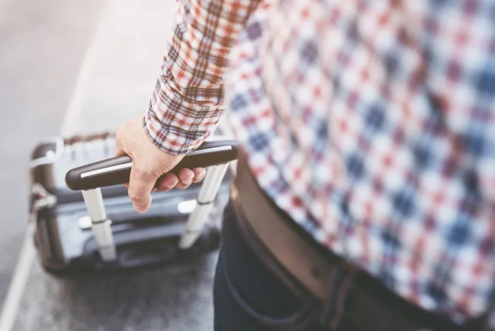 Man in plaid shirt pulling a rolling suitcase outdoors, close-up on handle.