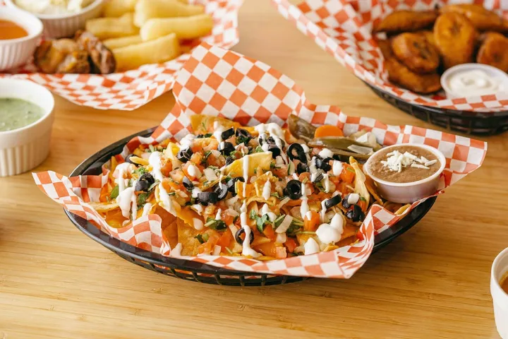 A loaded basket of nachos with toppings served at a casual restaurant with sides.