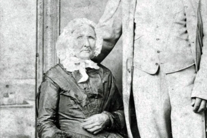 Vintage black-and-white portrait of an elderly woman seated beside a standing man.