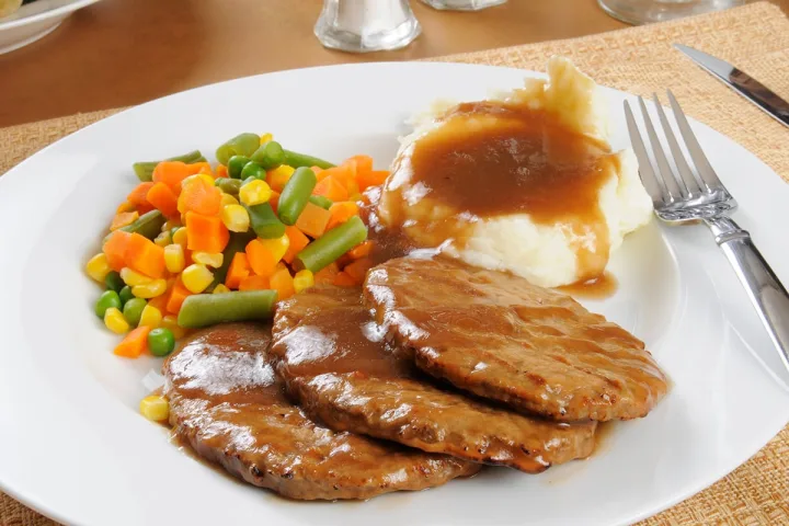 A plated meal of Salisbury steak with gravy, mashed potatoes, and mixed vegetables.