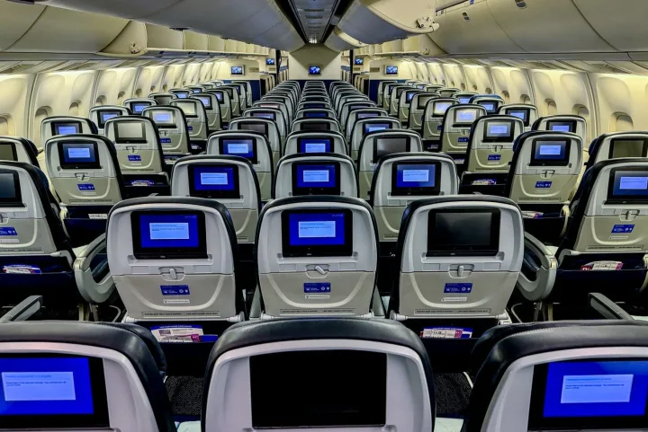 Empty rows of economy class seats with seatback screens inside a United Airlines cabin.