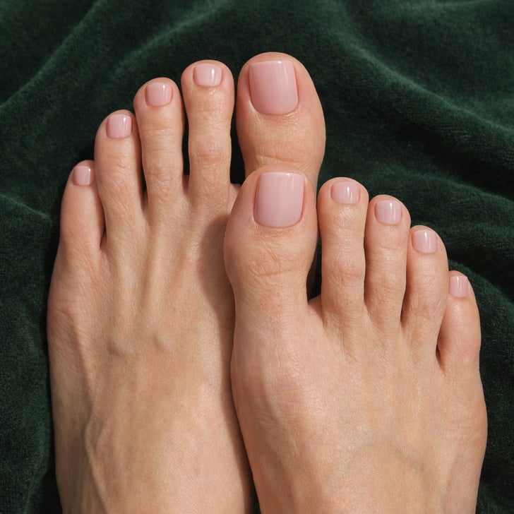 Feet with nude pink pedicure displayed on dark green velvet towel.