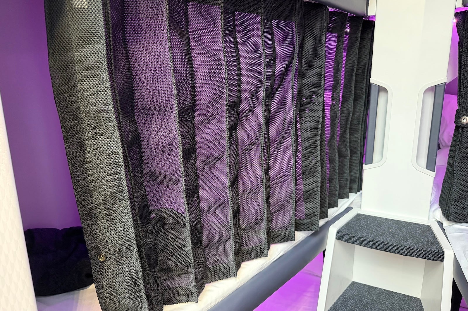 Close-up of closed black mesh privacy curtains on Air New Zealand Skynest sleep pods with purple ambient lighting.