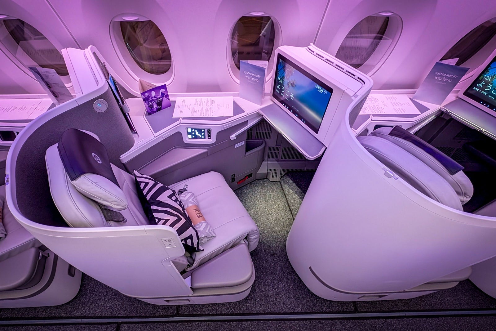 Fiji Airways business class cabin with white lie-flat seats, purple mood lighting, and entertainment screens.