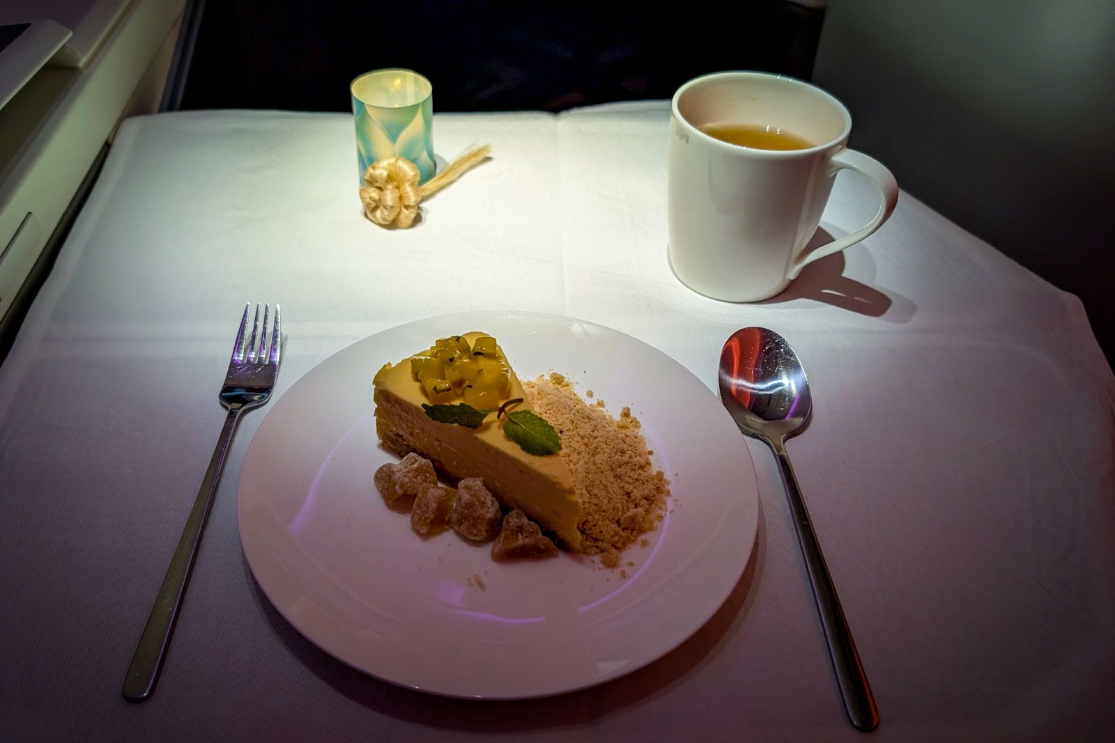 Elegant dessert slice with passionfruit topping and tea cup on a white tablecloth in a dim cabin setting.