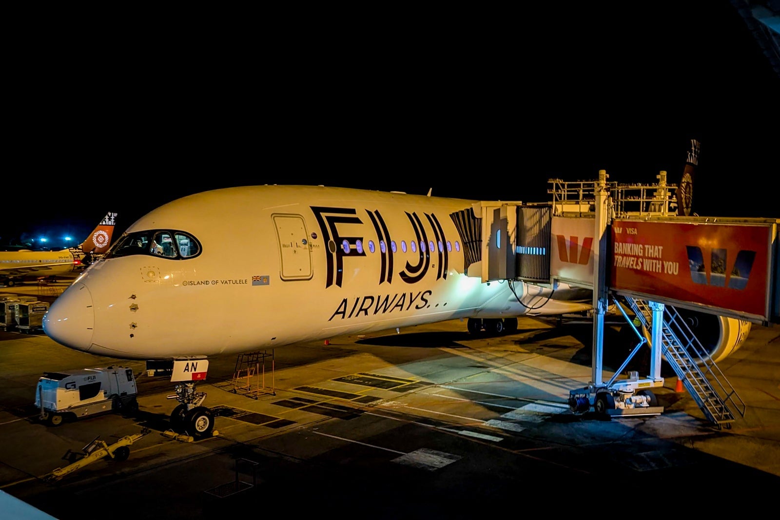 Fiji Airways aircraft parked at gate at night, fully illuminated on the tarmac.